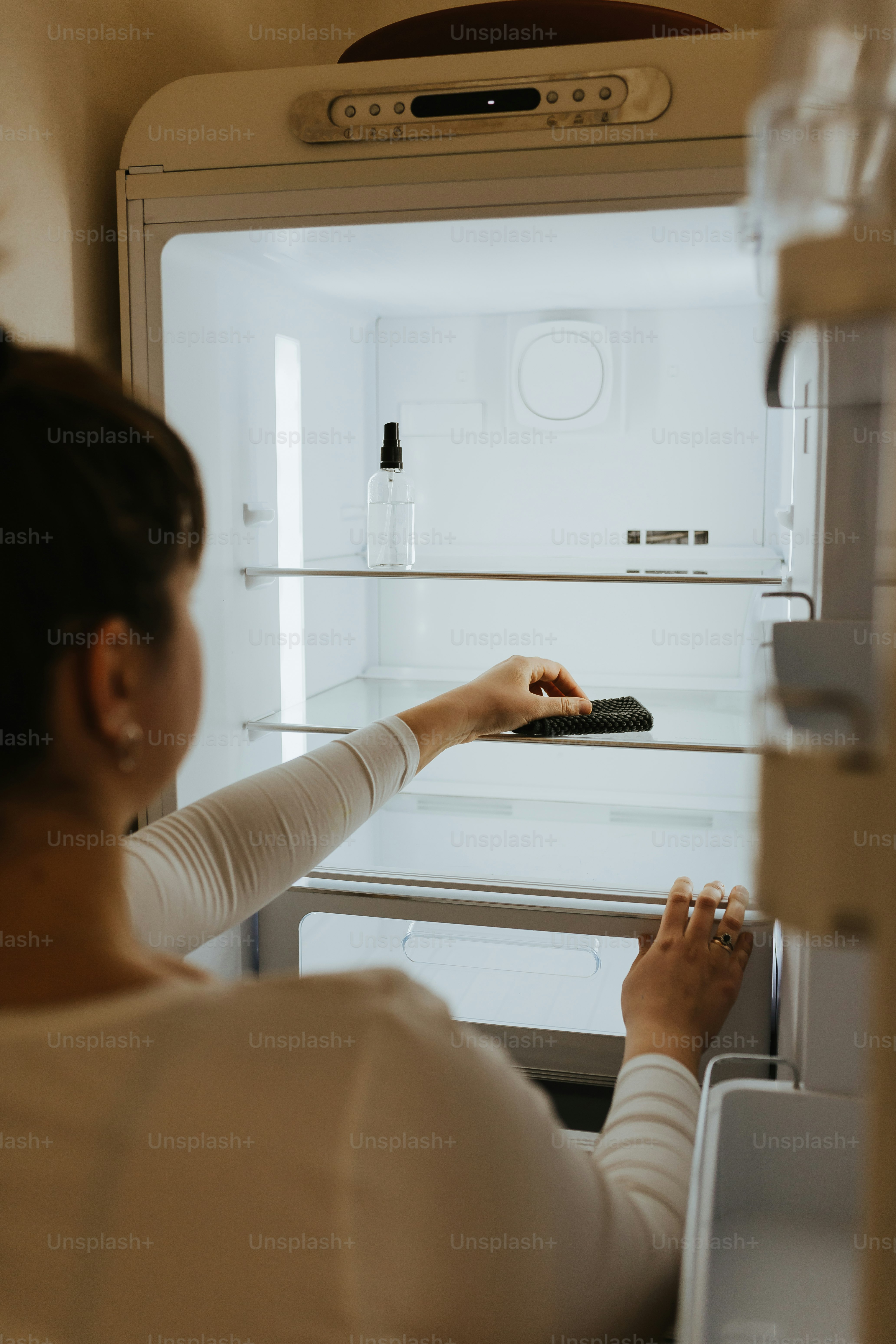 開いた冷蔵庫の前でリモコンを持つ女性