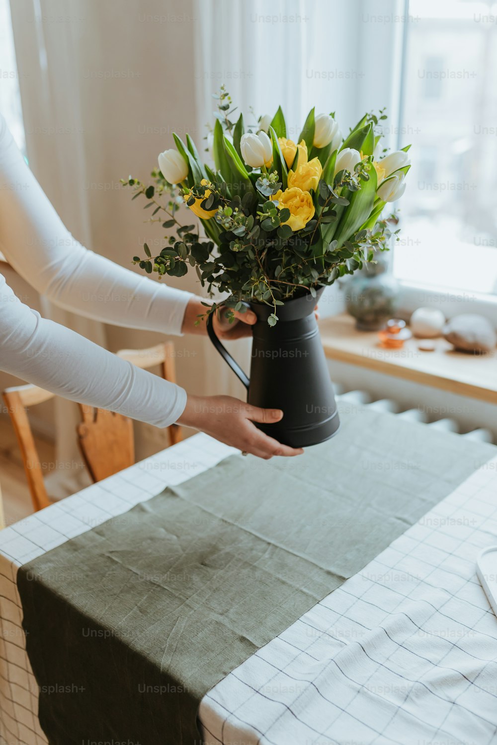 a person holding a vase with flowers on a table