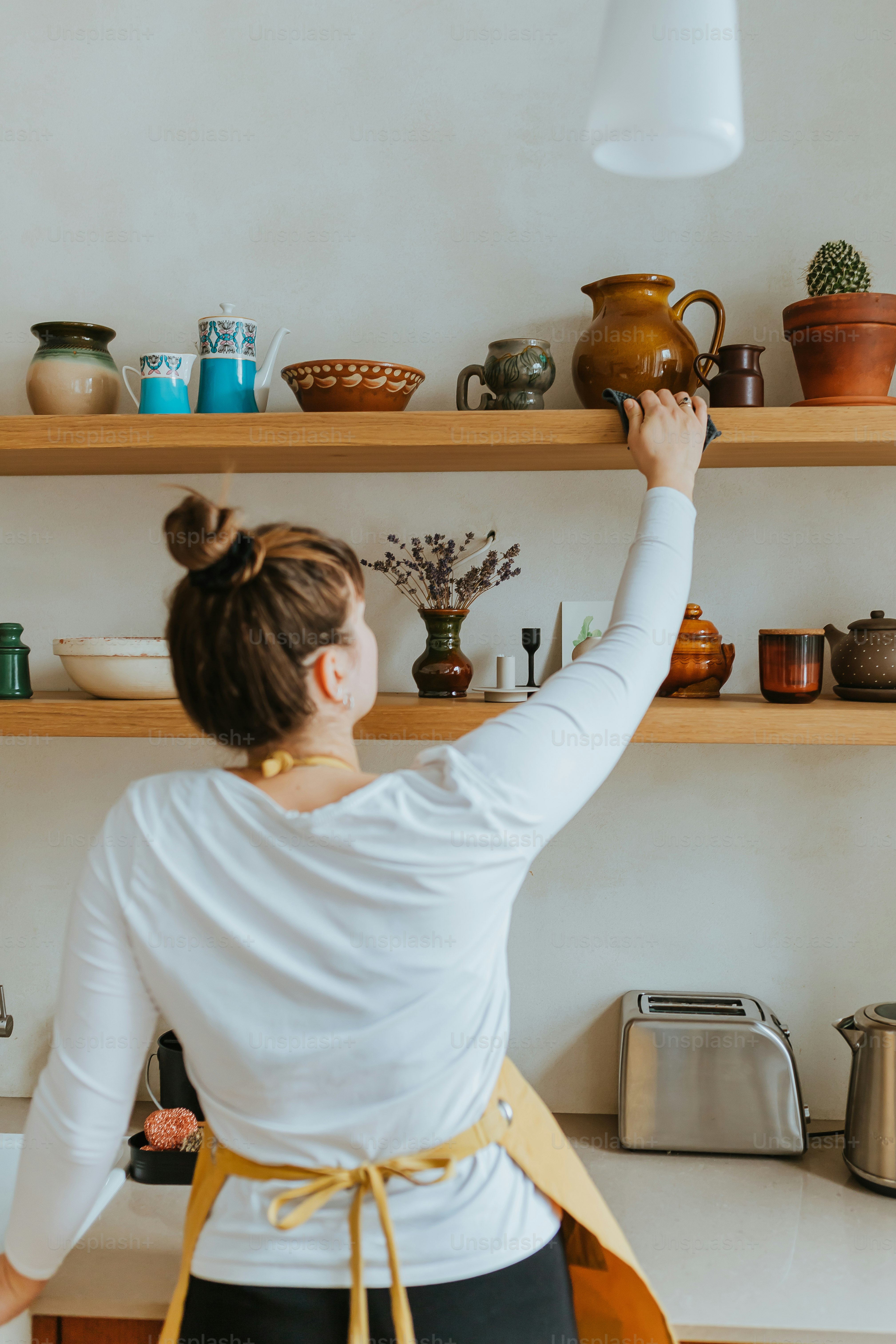 냄비로 가득 찬 선반 앞에 서 있는 여자