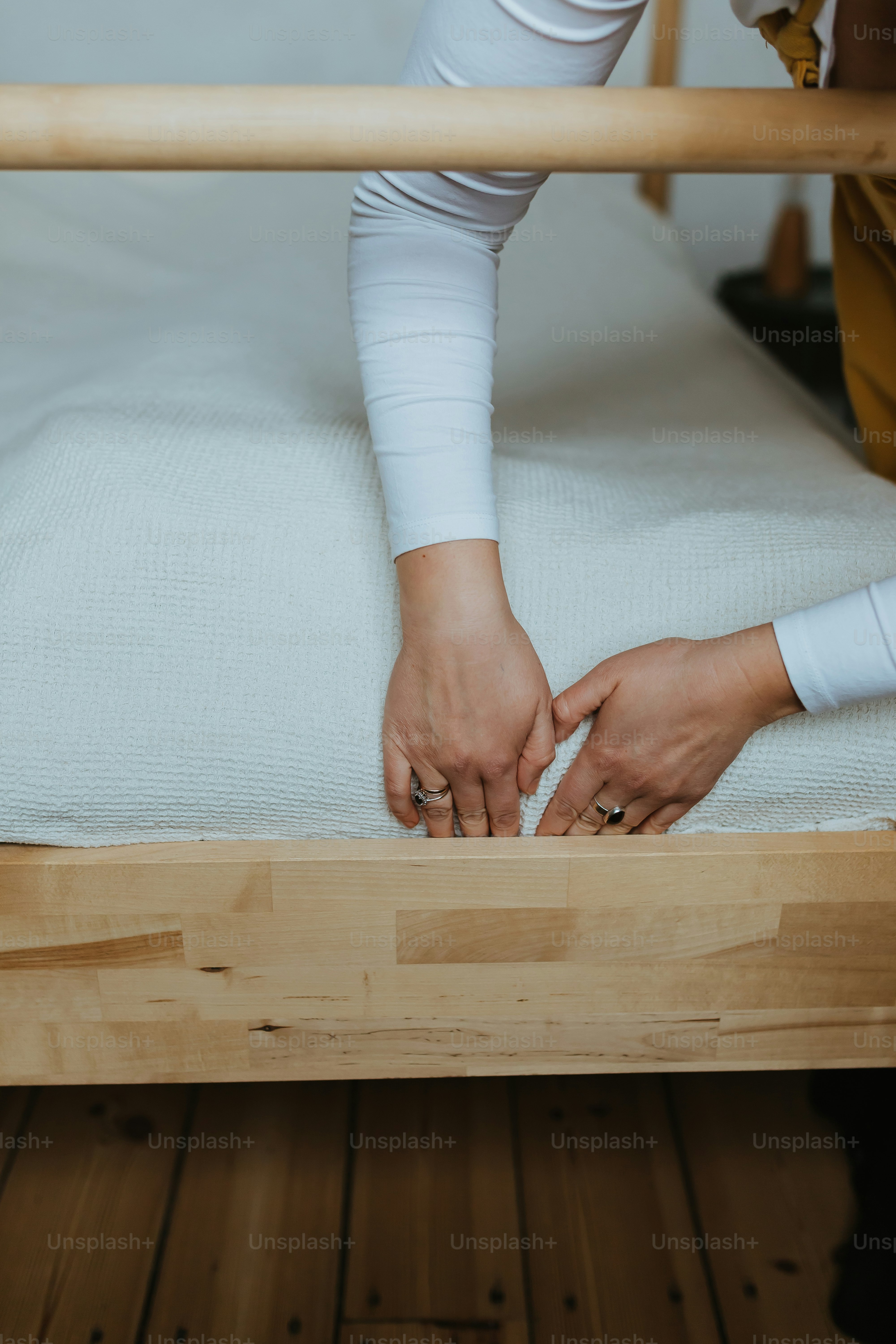 ベッドフレームのマットレスに手を伸ばす人