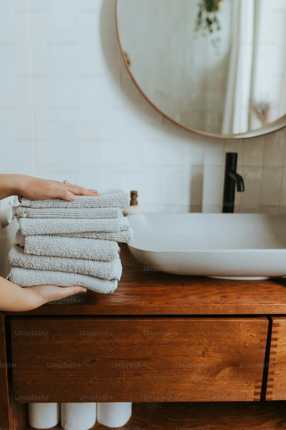 a person holding a stack of towels in front of a sink