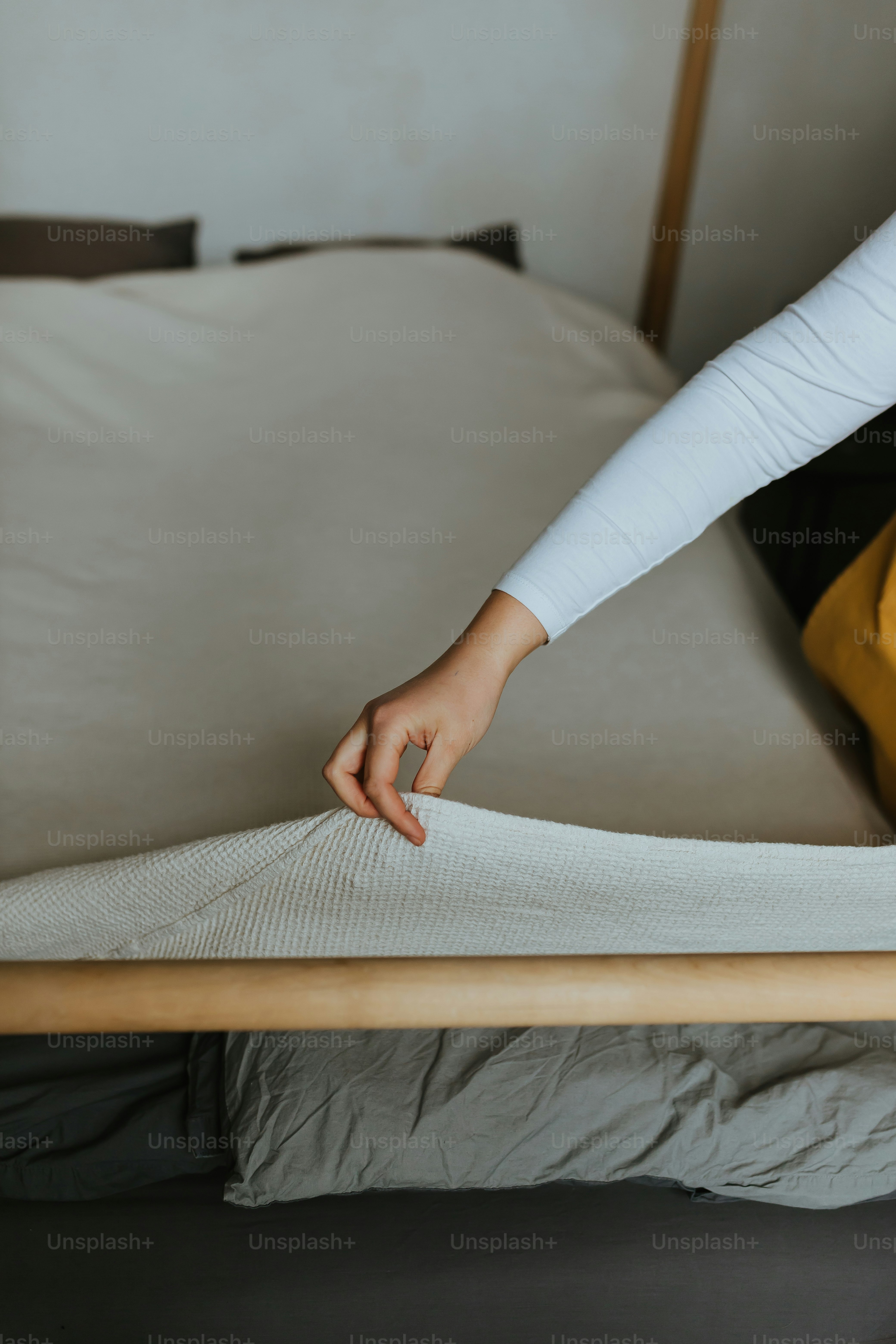 A woman putting a mattress on top of a bed photo Tidy Image on Unsplash
