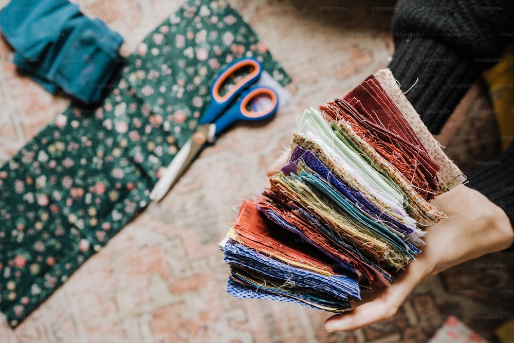 a person holding a stack of fabric next to a pair of scissors