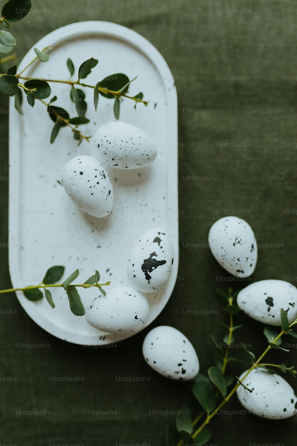 una bandeja blanca cubierta con huevos blancos junto a hojas verdes