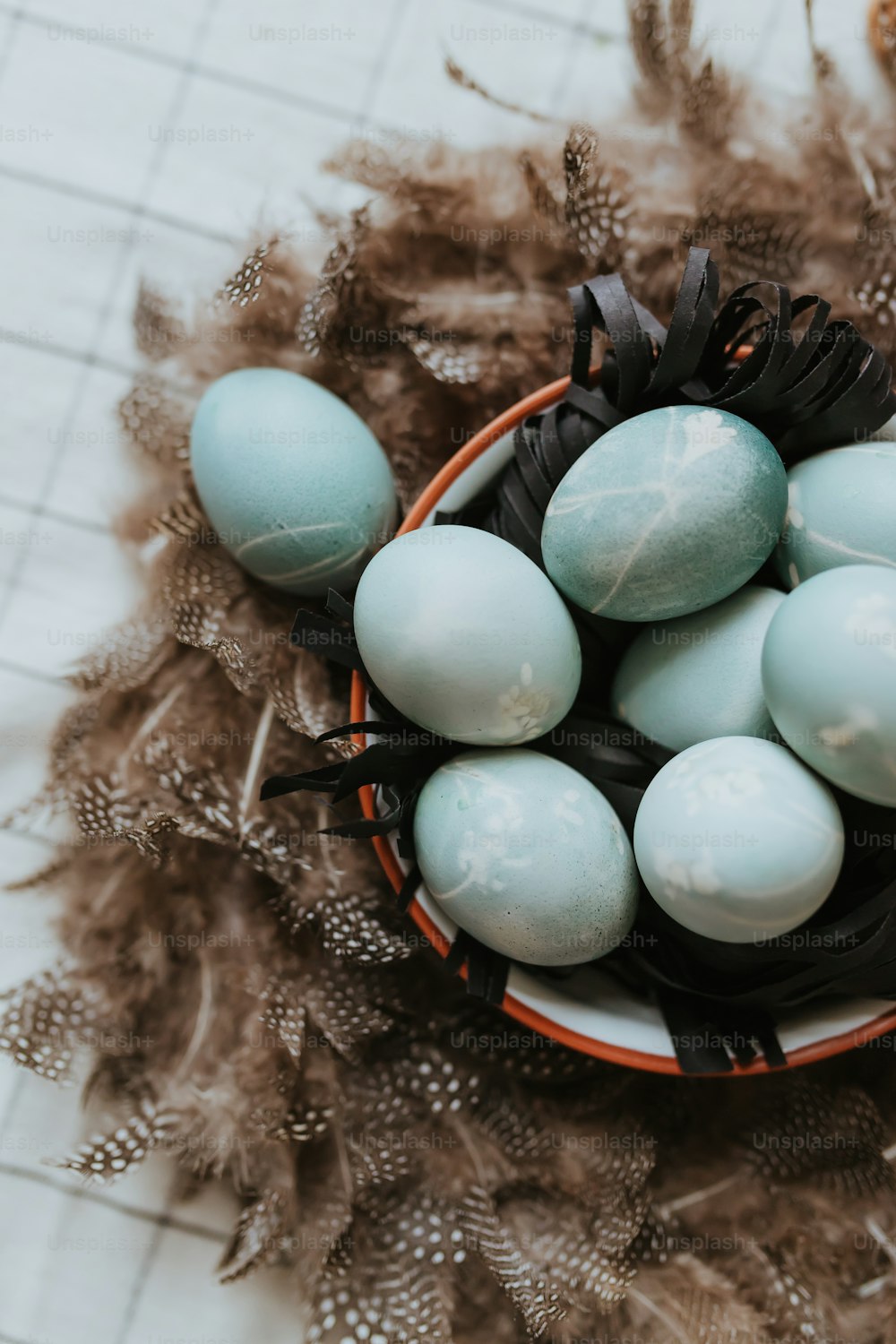 a basket filled with blue eggs on top of feathers