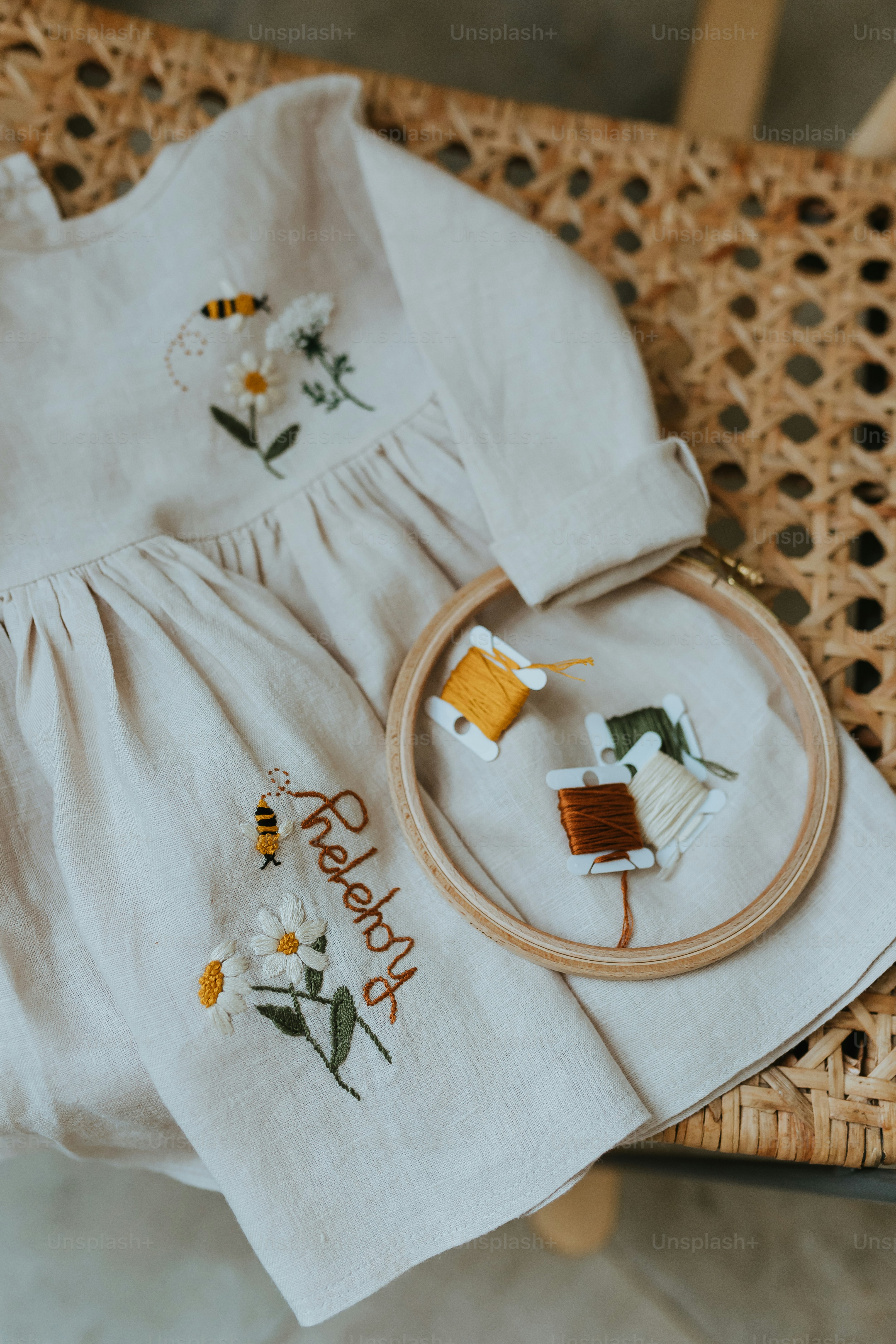 un vestido de bebé y un kit de punto de cruz sentado en una silla de mimbre