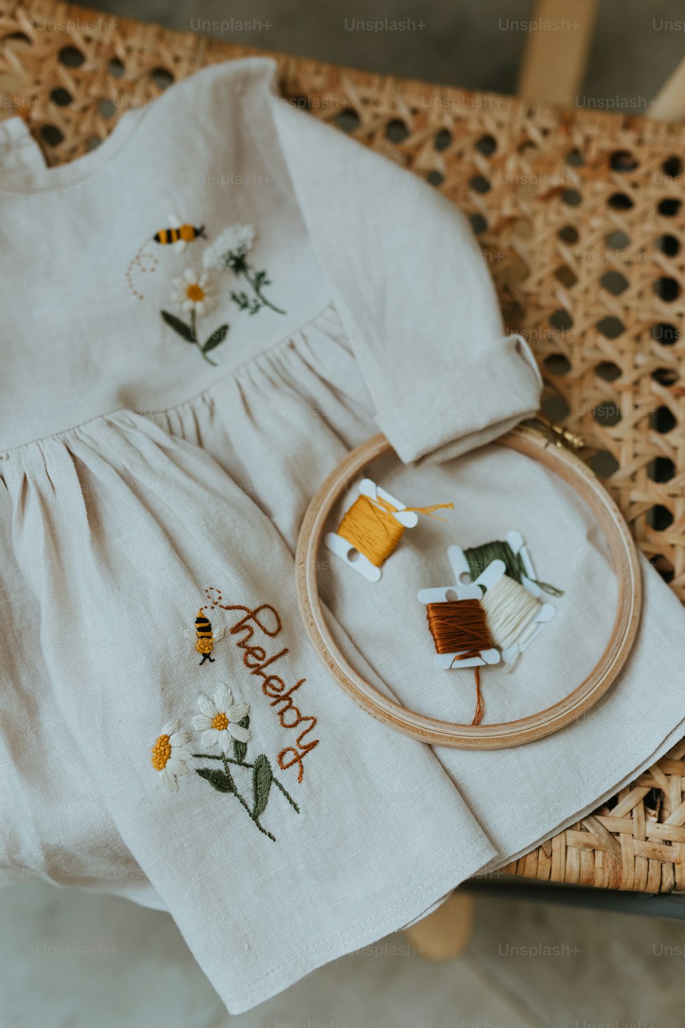 a baby's dress and a cross stitch kit sitting on a wicker chair