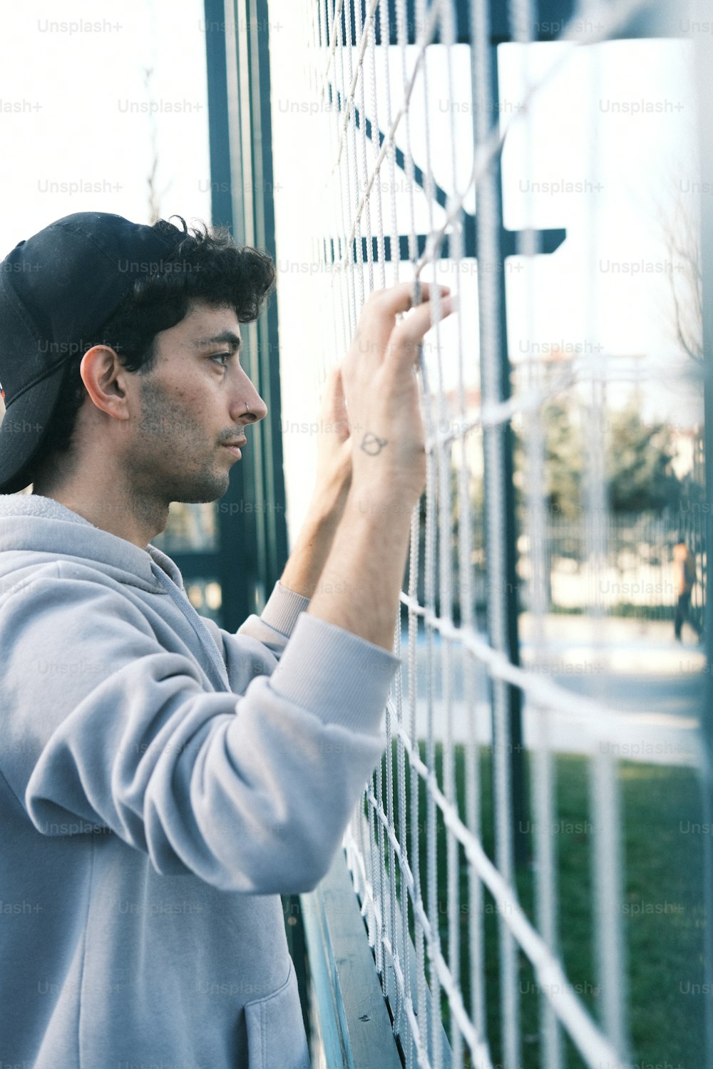 a man leaning against a fence with a baseball cap on