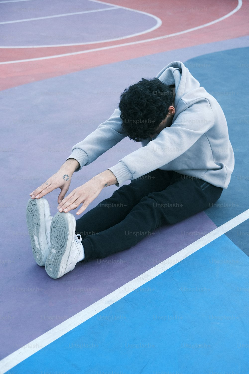 足を地面につけてバスケットボールコートに座っている男性
