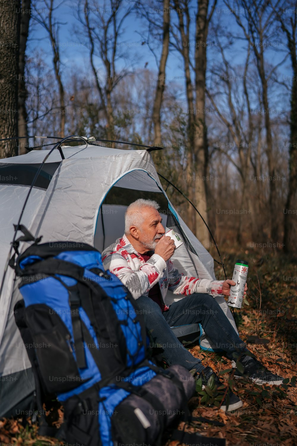 a man sitting next to a tent in the woods