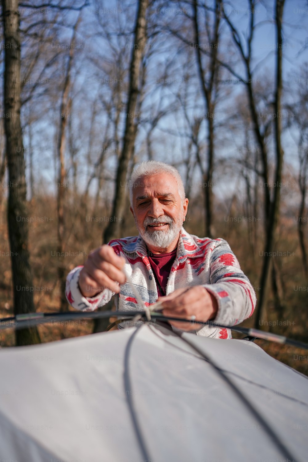Ein älterer Mann hält sich im Wald an einem Segel fest