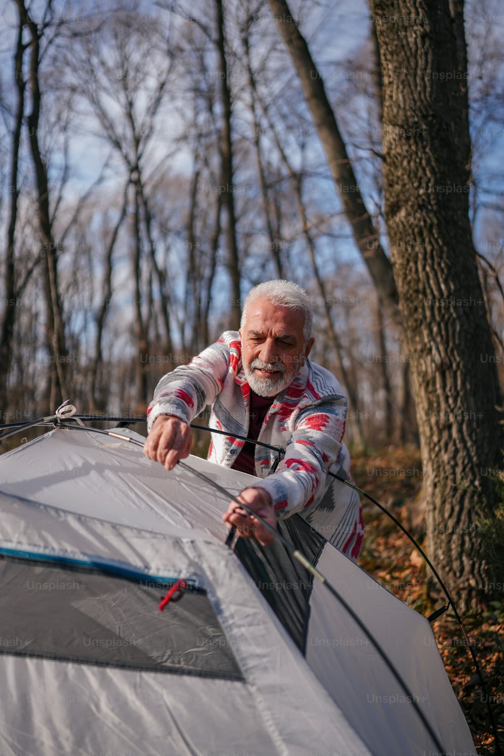 Ein älterer Mann baut im Wald ein Zelt auf