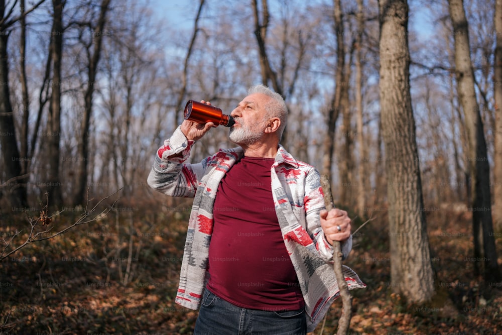 Un uomo in piedi nel bosco che beve da una bottiglia