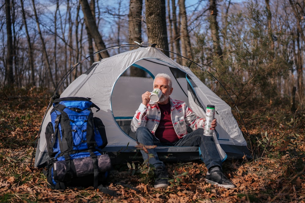 a man sitting in front of a tent drinking from a cup