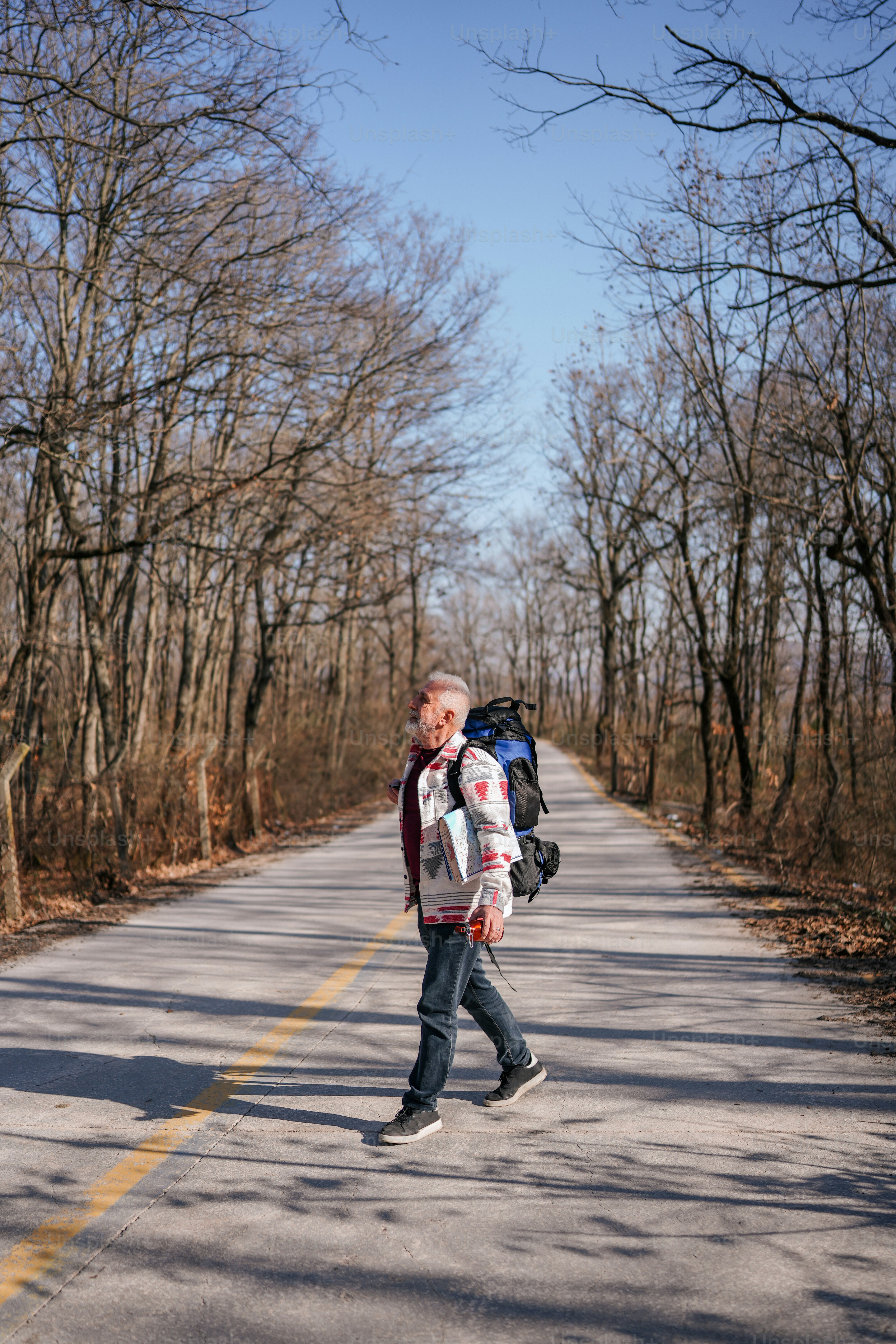 A man walking down a road with a backpack on his back photo – Senior ...