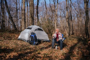 a man sitting next to a tent in the woods