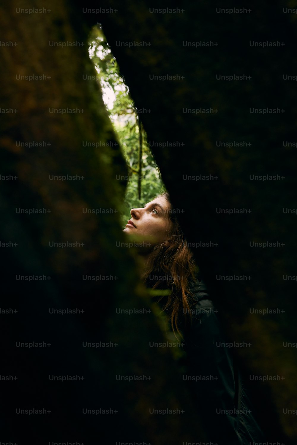 a woman standing in the woods looking up at something