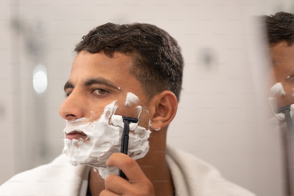 um homem raspando o rosto na frente de um espelho