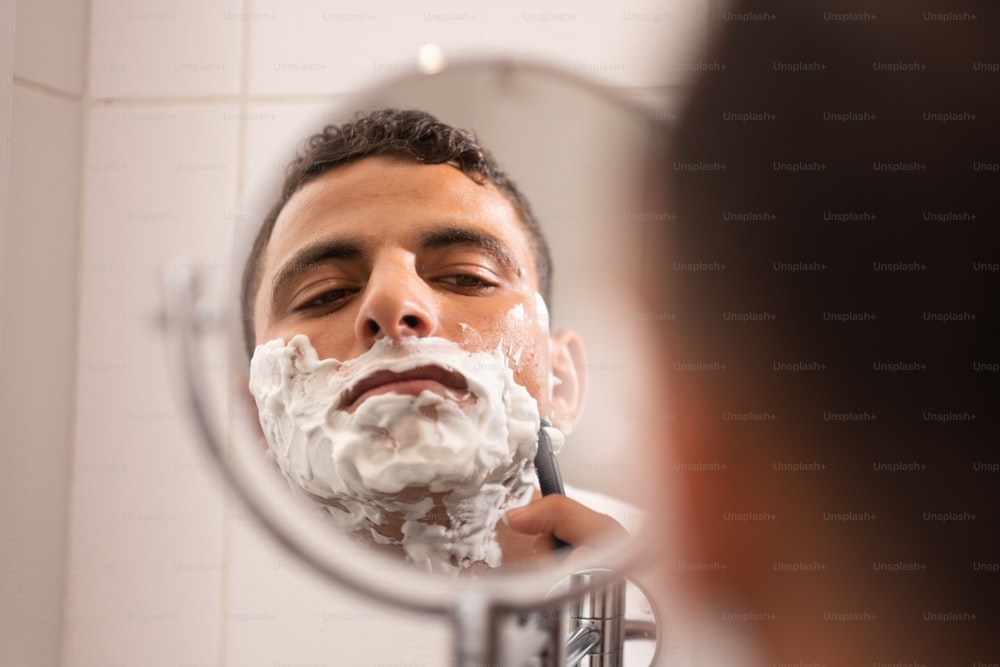 a man shaving his face in front of a mirror