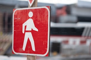um sinal de pedestre vermelho e branco em um poste de madeira