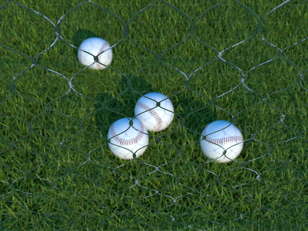 four baseballs are sitting in the grass behind a fence