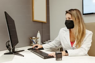 a woman wearing a face mask sitting at a desk in front of a computer