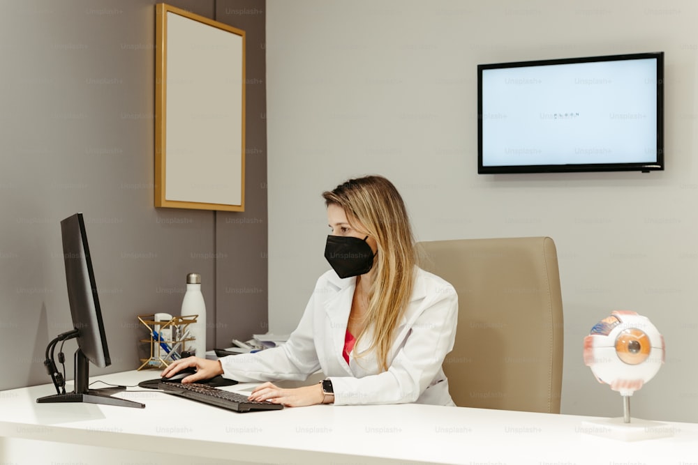 a woman sitting at a desk wearing a face mask