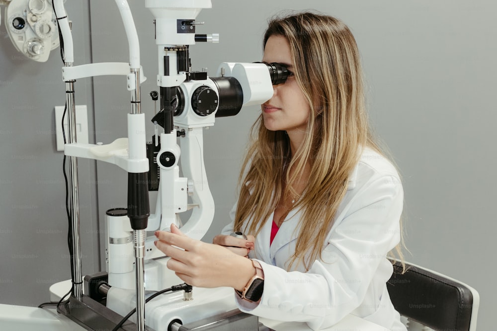 uma mulher em um jaleco branco olhando através de um microscópio