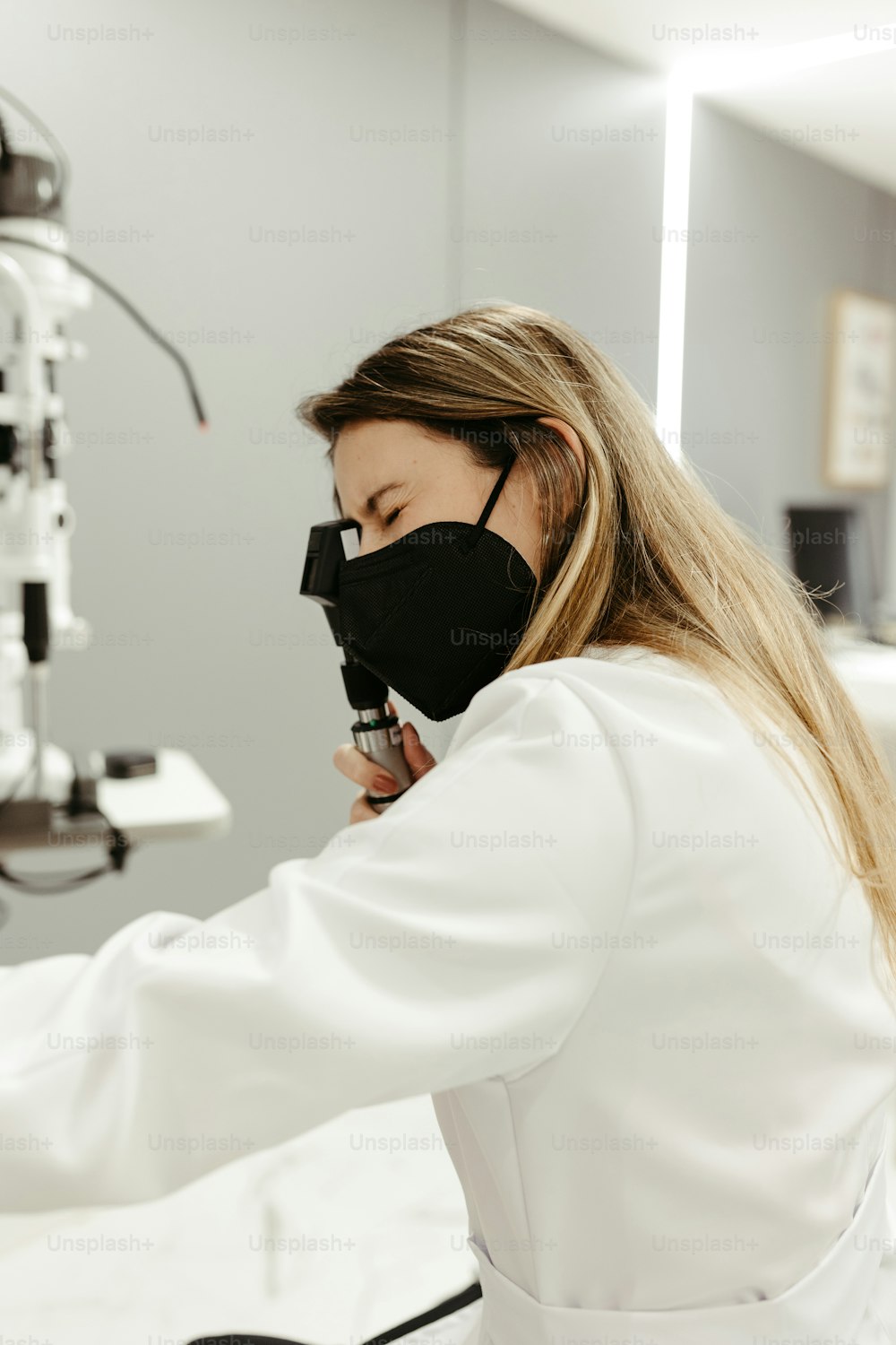 Eine Frau im weißen Laborkittel schaut auf ein Mikroskop
