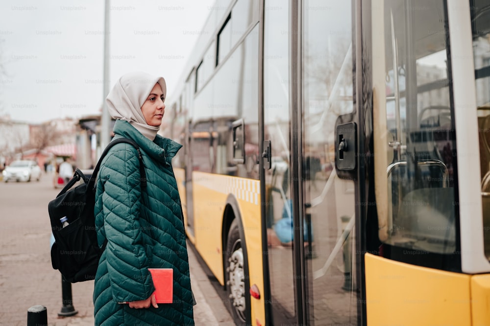 a woman in a hijab stands in front of a bus