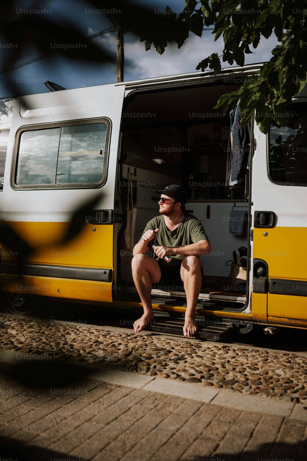 um homem sentado em um banco na frente de um ônibus amarelo e branco