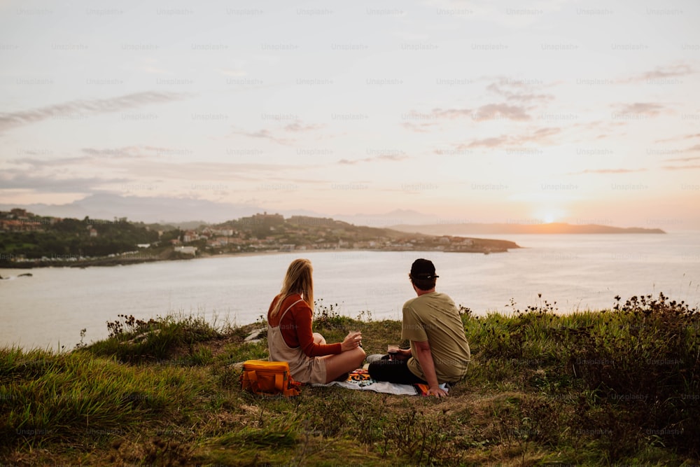 Ein Mann und eine Frau sitzen auf einem Hügel mit Blick auf ein Gewässer