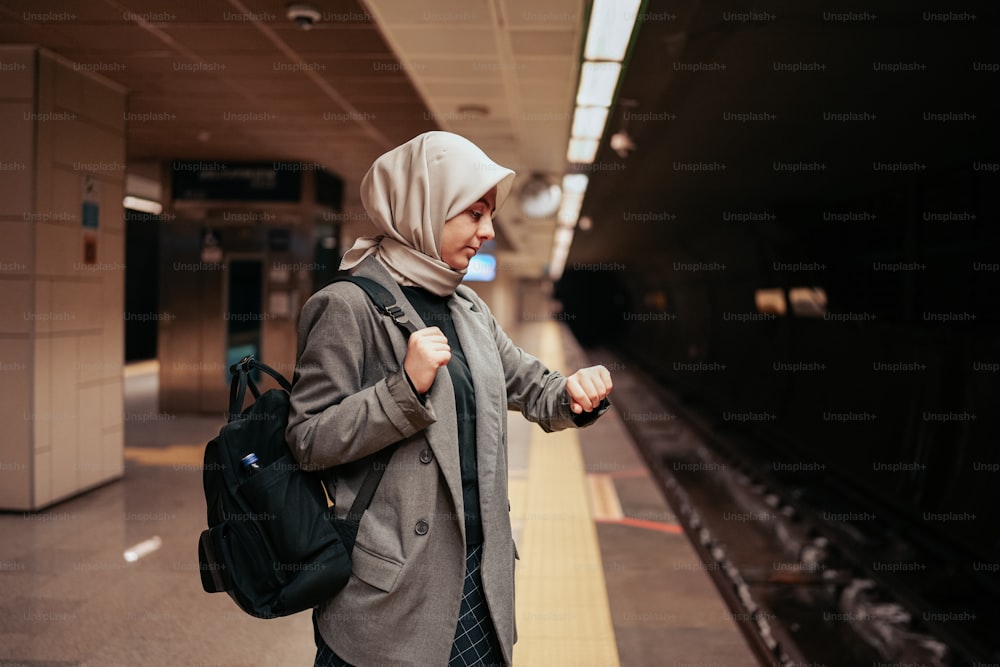 uma mulher em um hijab fica em uma estação de trem