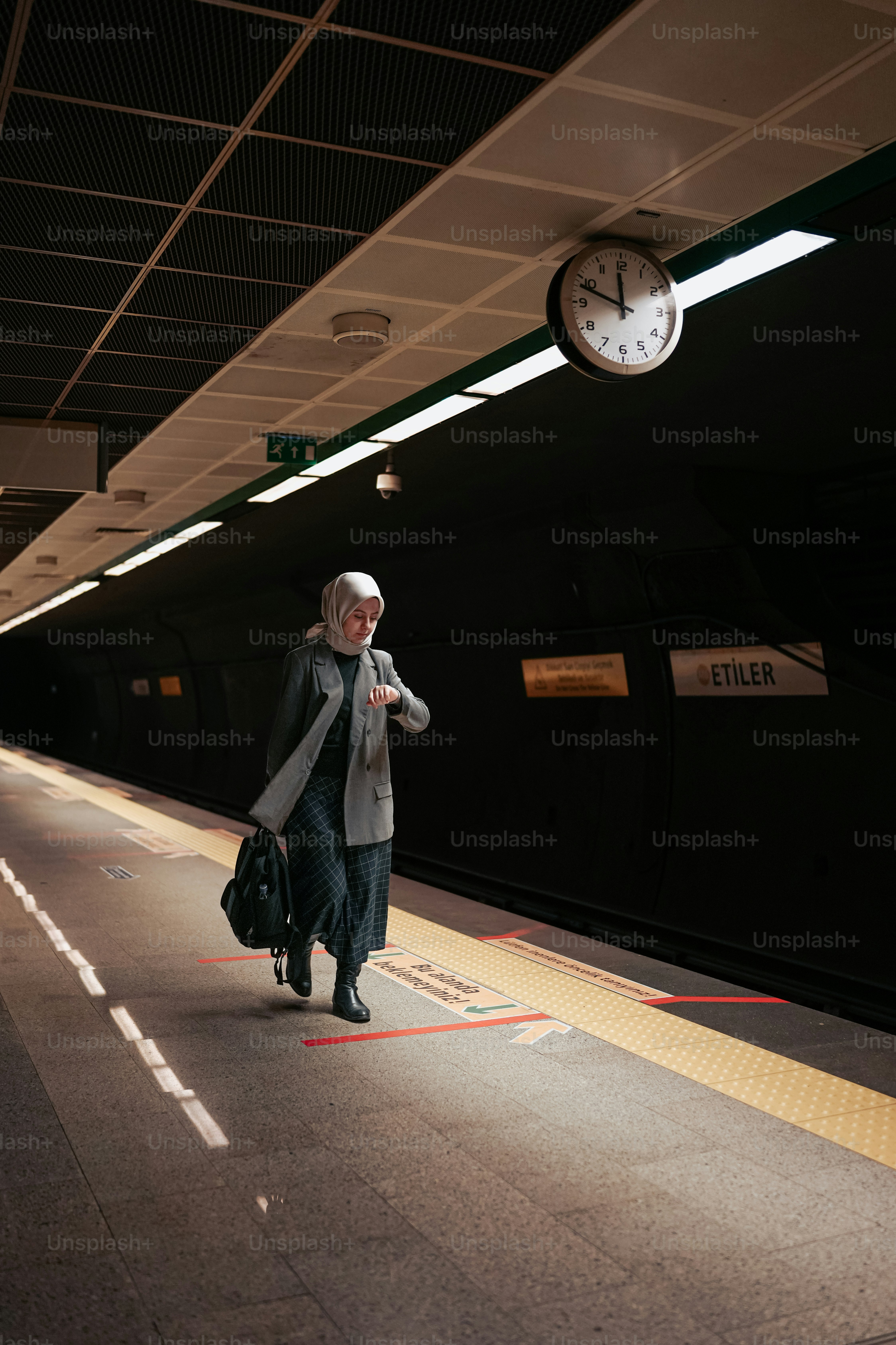 a woman walking down a train platform next to a clock
