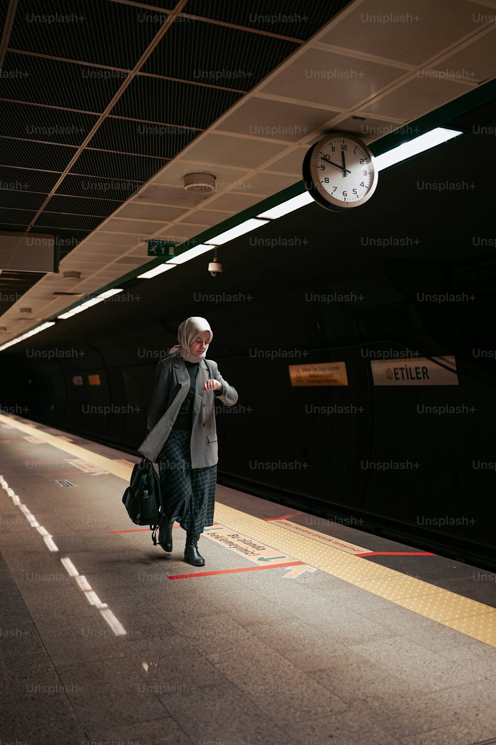 時計の隣の電車のプラットホームを歩いている女性