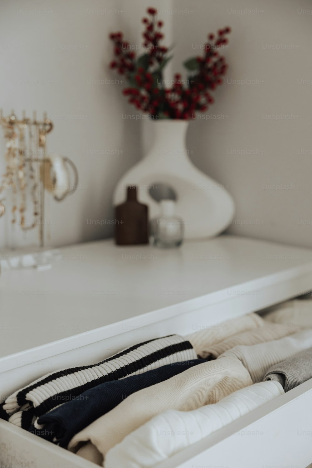 a white dresser with clothes in it and a vase with flowers