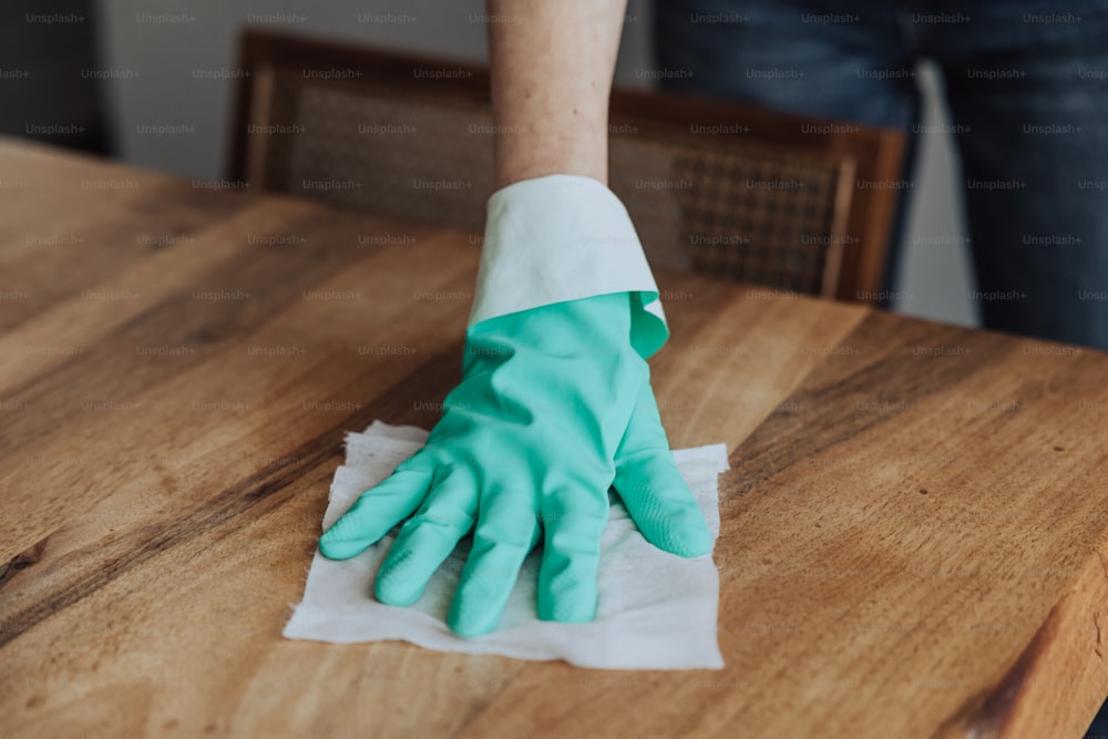 Eine Person, die einen Holztisch mit einem grünen Handschuh reinigt
