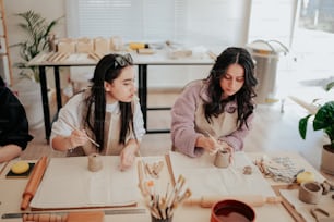 two women sitting at a table working on crafts