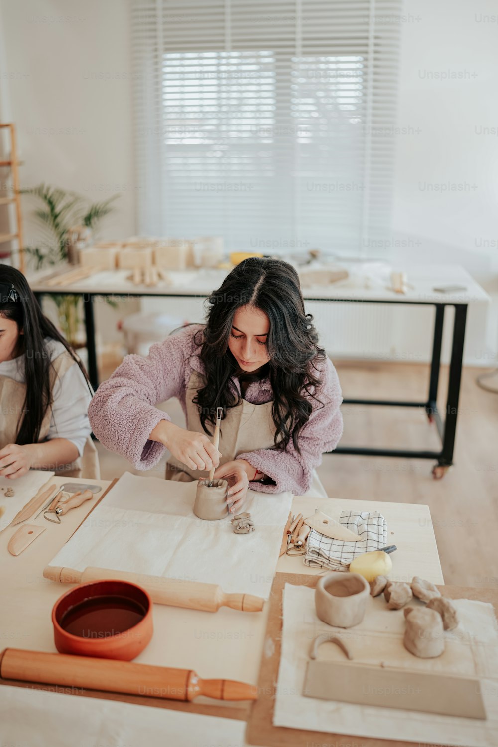 two women sitting at a table working on pottery