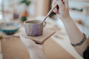 a woman is painting a cup with a brush