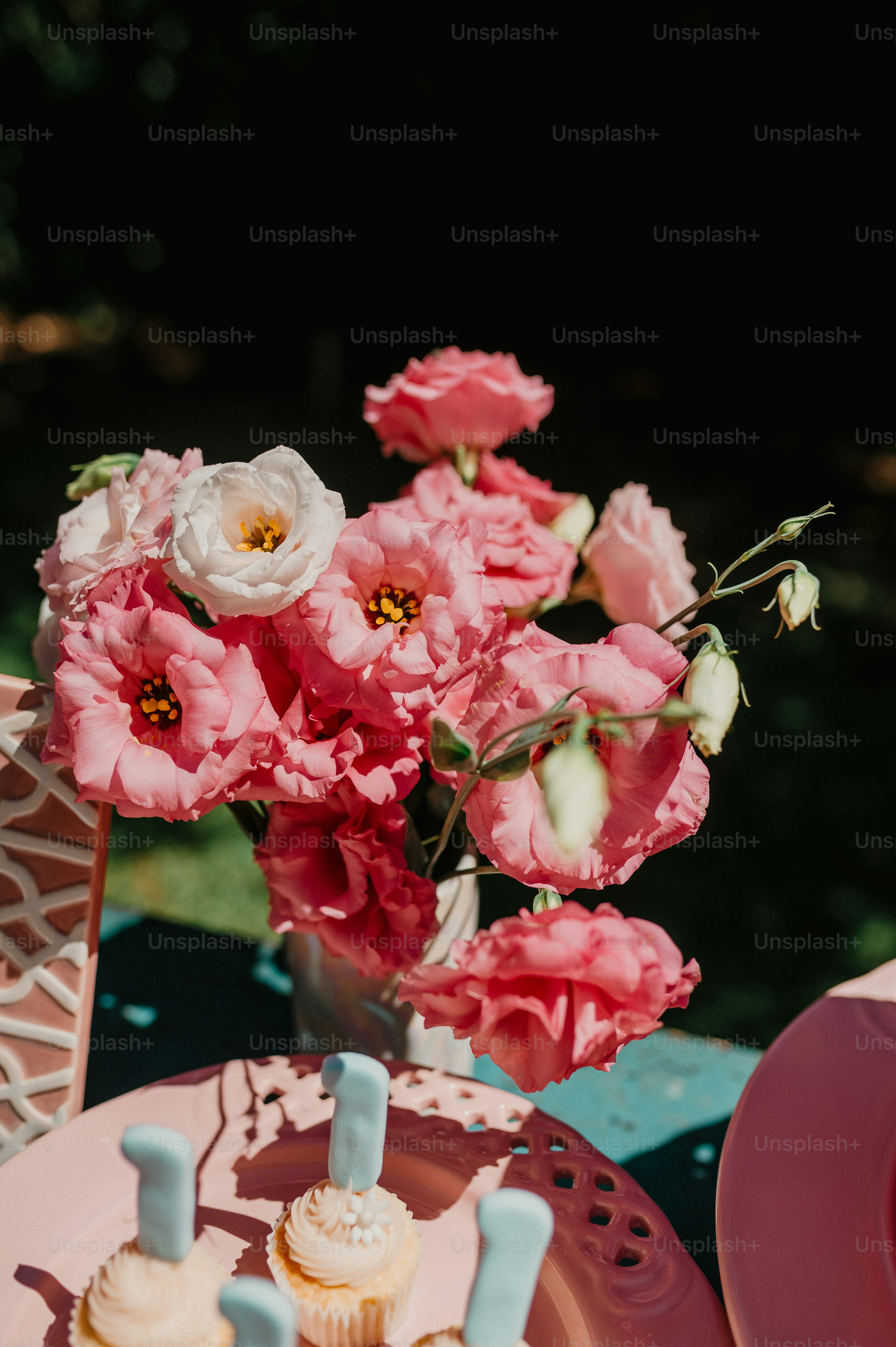 a vase filled with pink flowers next to cupcakes