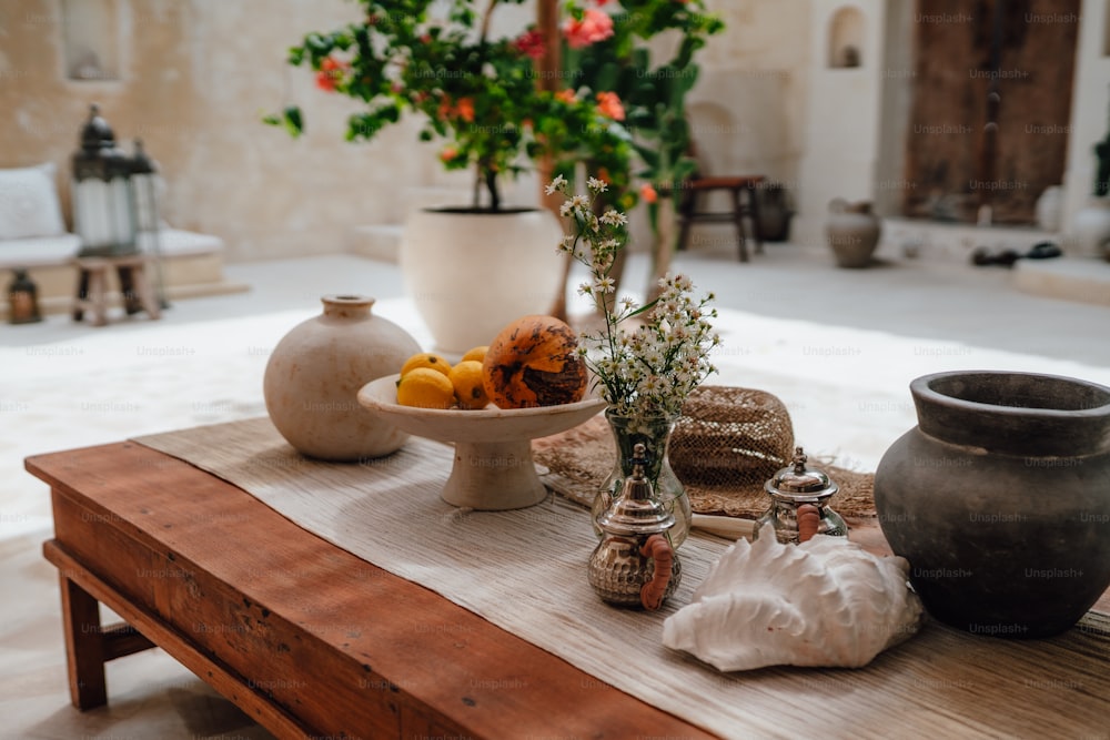 a wooden table topped with a bowl of fruit and vases