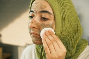 a woman with a green scarf on her head holding a white towel to her face