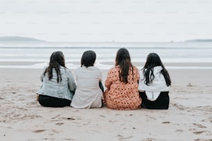 three girls sitting on the beach looking out at the ocean