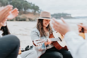 a woman sitting on a beach playing a guitar