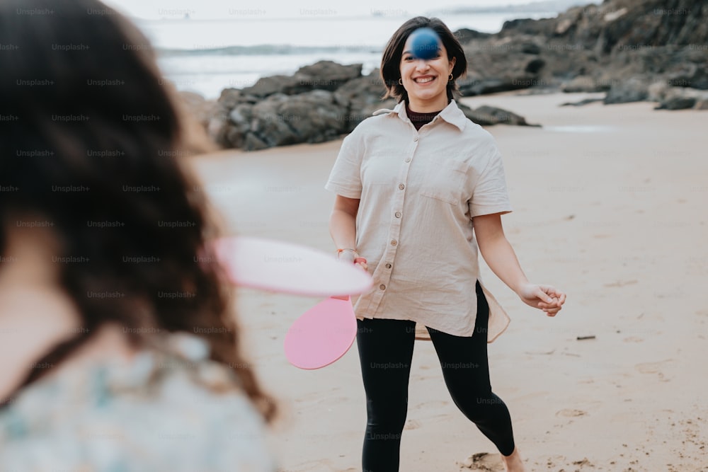 Eine Frau, die an einem Strand steht und einen rosa Frisbee hält