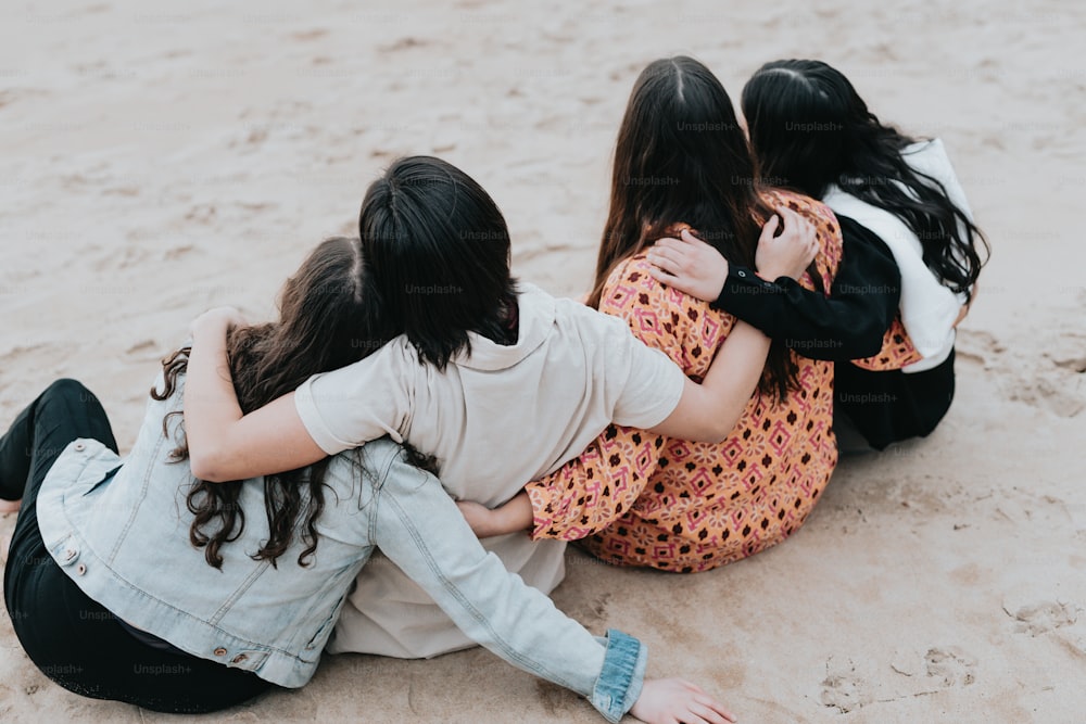 a group of girls sitting on top of a sandy beach