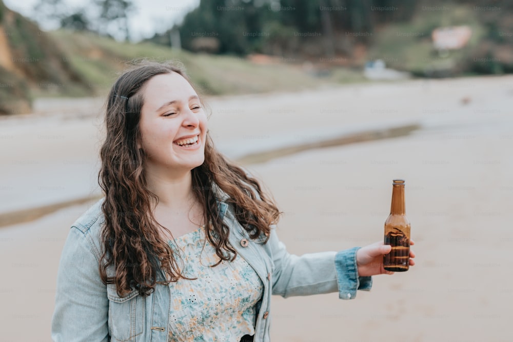 a woman holding a bottle of beer on a beach