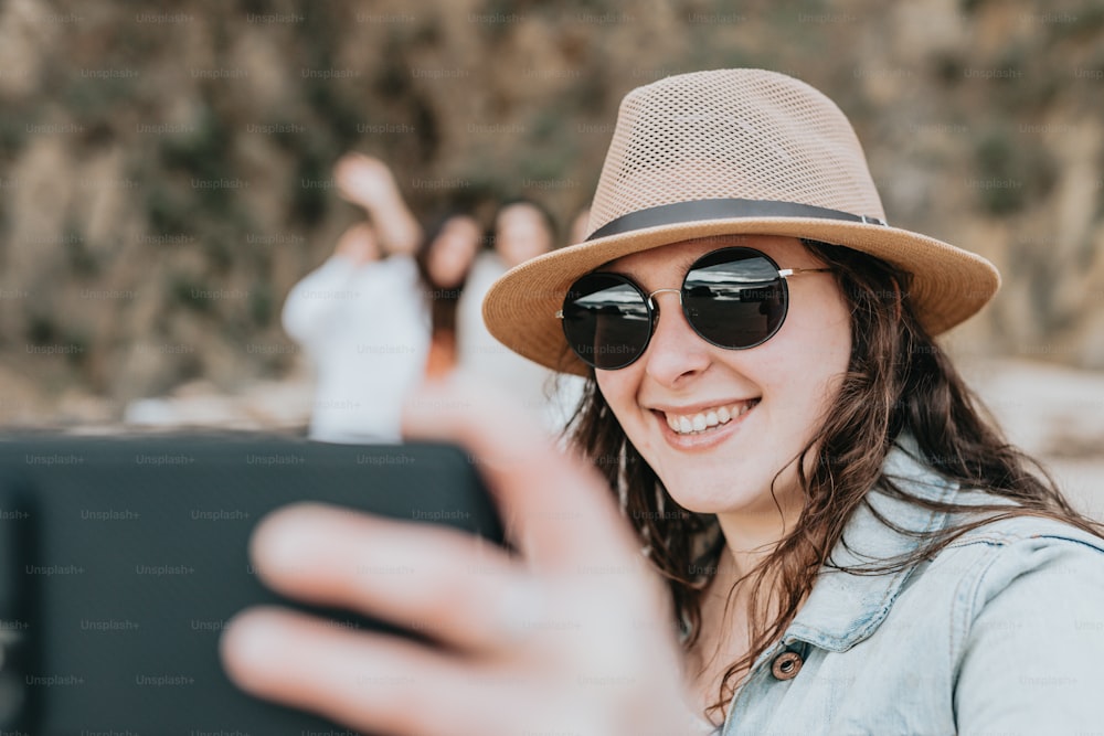 a woman wearing a hat and sunglasses taking a picture with her cell phone