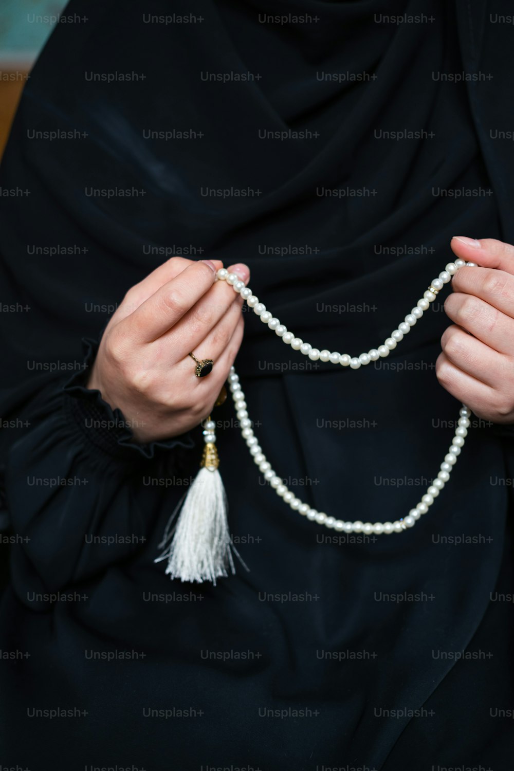 une femme vêtue d’une tenue noire tenant un collier de perles blanches